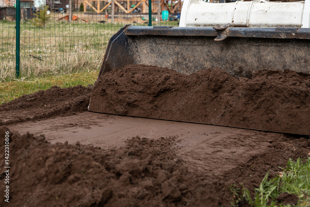 A bulldozer pushes soil across the ground in a fenced area. Blurred structures and construction materials are visible, highlighting earthmoving activity.