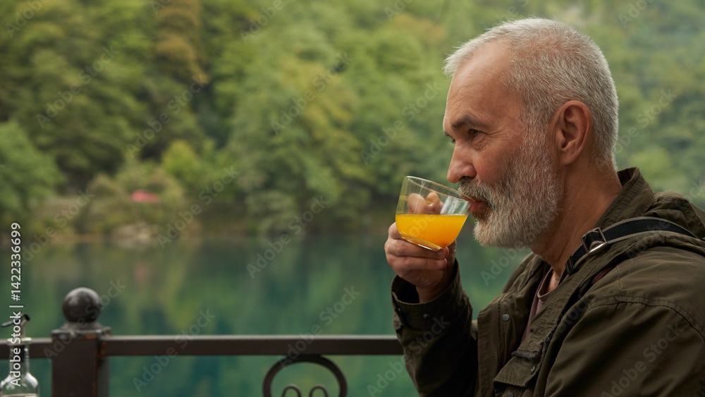 A grown man with a cup of sea buckthorn tea in a summer cafe on the shore of a picturesque mountain lake.