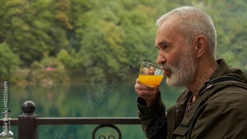 Obraz na płótnie A grown man with a cup of sea buckthorn tea in a summer cafe on the shore of a picturesque mountain lake. w salonie