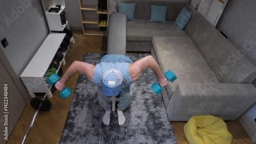  Young athlete pumps up the deltoid muscle of the shoulder with dumbbells at home, home workout in modern apartments. Exercise with dumbbells. Slow motion.