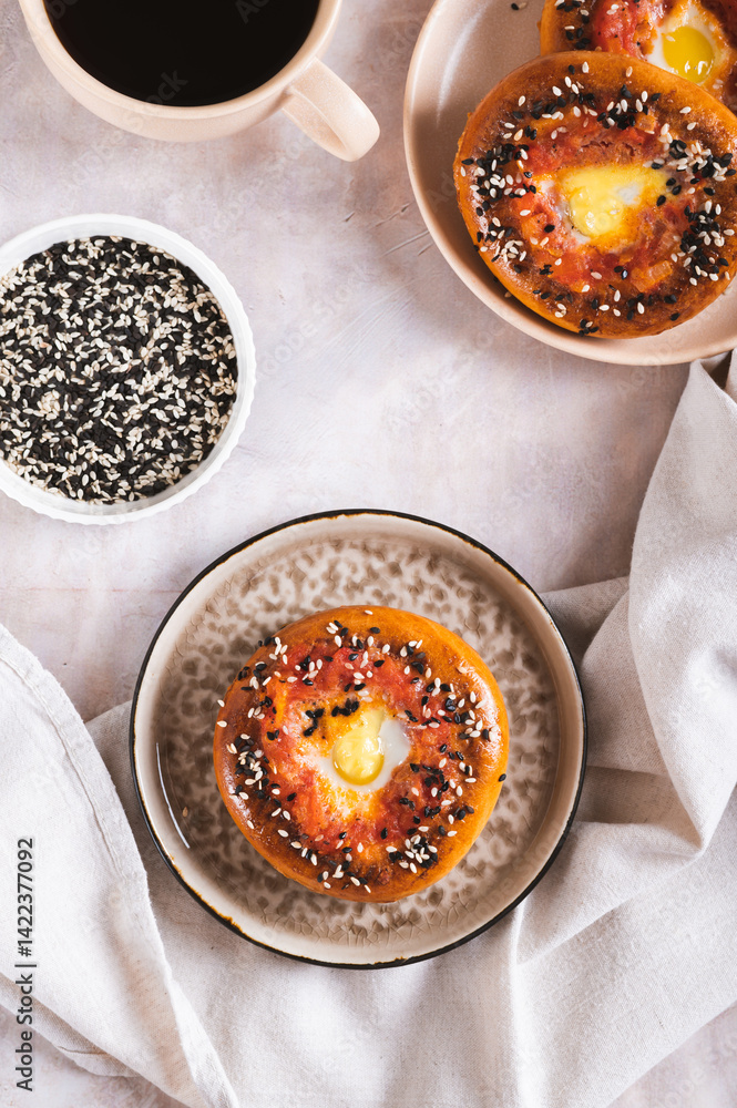 Egg with tomato and sesame seeds baked in bagels on a plate top and vertical view