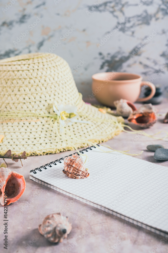 Travel planning notebook, hat, seashells and cup of coffee on table vertical view