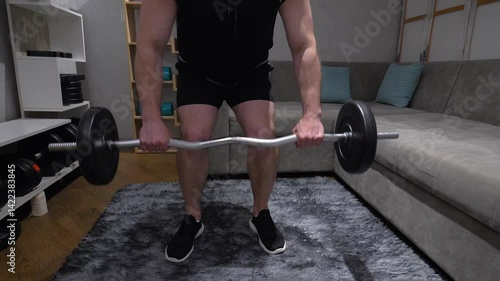 Male athlete in sportswear with a rod with heavy weight in hands. Workout at home with weights. Pumping up the shoulder and back muscles. Close-up. Slow motion