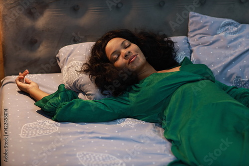 Curly young woman in green dress sleeping on bed