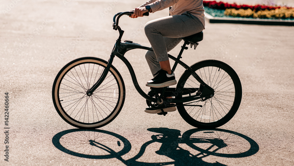 Fototapeta premium Urban style, way to work and eco transport in modern city. Millennial man employee or businessman rides on bike in city in summer park, with shadow on road, outdoor, side view, free space, cropped