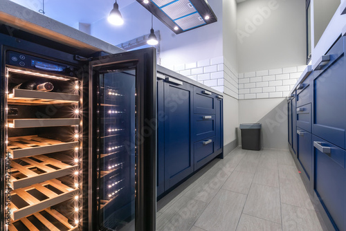 Fotografija A modern kitchen with elegant blue furniture and a wine cooler that emphasizes the sleek design, ample storage space and modern lighting