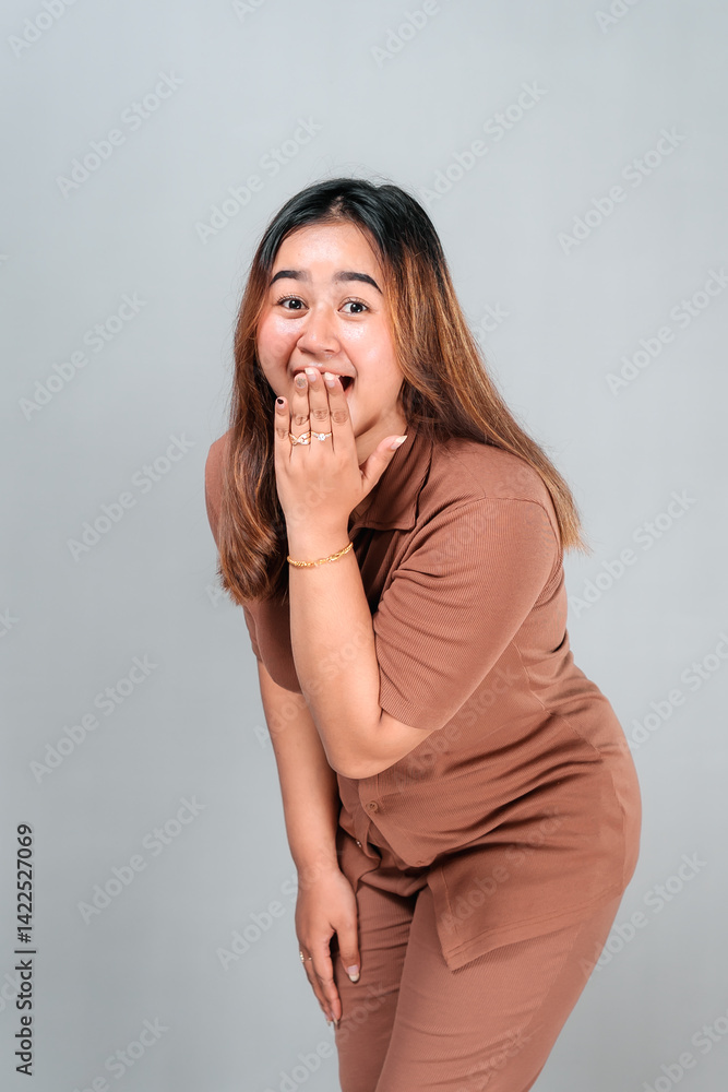 Portrait of a young woman showing a surprised facial expression with wide eyes and hand covering her mouth. Her playful gesture and emotional reaction convey shock and amusement. Portrait of a young woman showing a surprised facial expression with wide eyes and hand covering her mouth. Her playful gesture and emotional reaction convey shock and amusement.