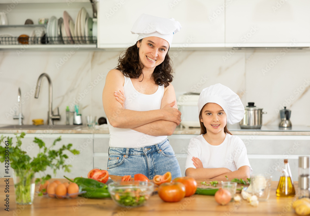 Mother with little girl in white cooking hats posing in kitchen, cooking class for small child. Mother with little girl in white cooking hats posing in kitchen, cooking class for small child.