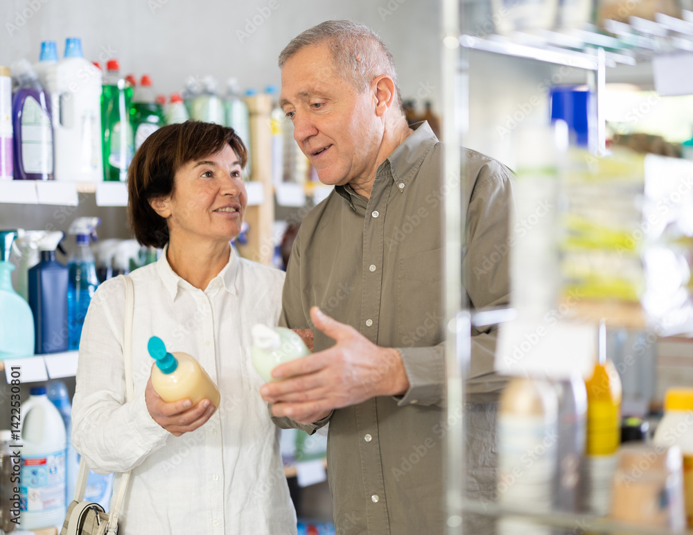 Fototapeta premium Elderly husband and wife choose a moisturizing liquid hand soap in the supermarket. Pensioners in a household store buy cream soap with a natural composition