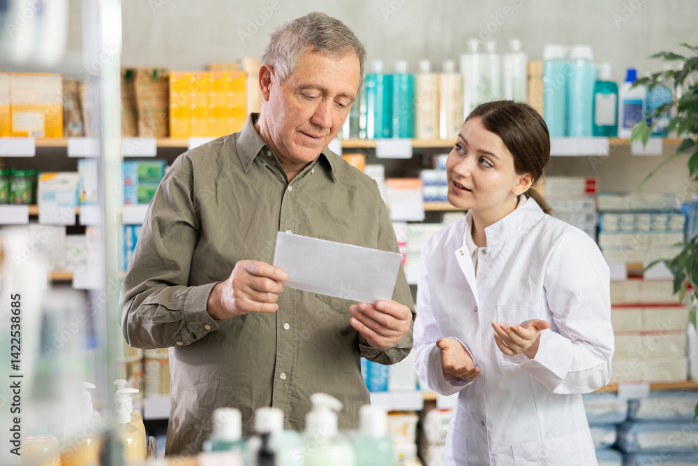 Obraz premium Elderly man choosing prescription medications with help of young female pharmacist in pharmacy