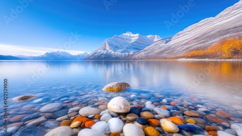 Serene mountain lake scene with colorful stones.  A tranquil lake reflects the majestic mountains.  Autumnal colors meet winter's chill in a breathtaking panorama