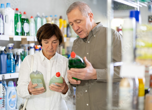 Obraz na płótnie Couple elderly man and woman buyers choosing dishwashing detergent in household chemicals store w salonie