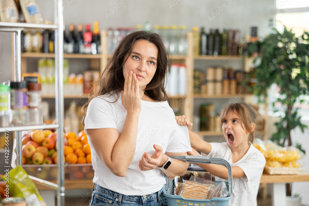 Capricious daughter screams and demands to buy sweets at the store. Mom is shocked by naughty child