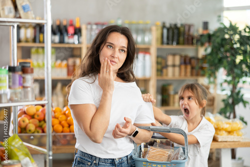 Obraz na płótnie Capricious daughter screams and demands to buy sweets at the store. Mom is shocked by naughty child w salonie