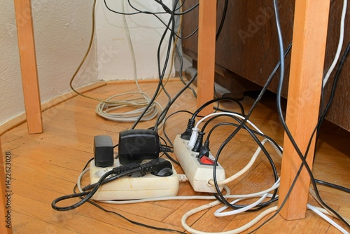 Tangled cables on the parquet floor. Overloaded electrical boards on the wooden floor. Electrical cables in disorder.