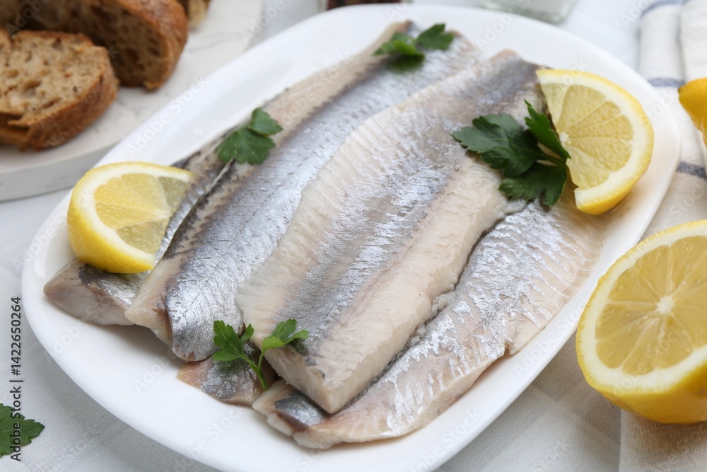Marinated herring fillets with lemon and parsley on white tiled table, closeup Marinated herring fillets with lemon and parsley on white tiled table, closeup