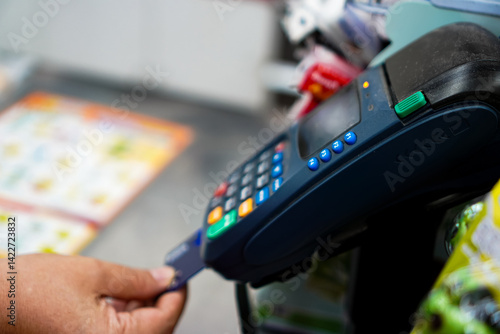 Photo of a person swiping a credit card through a Mobile EDC machine in a convenience store,  Thailand.