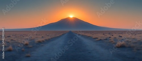 Sunset over a distant mountain, seen from a long dirt road.