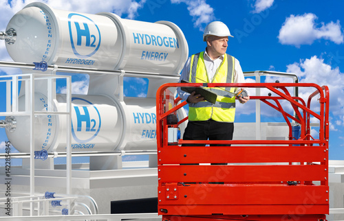 Man is specialist in hydrogen energy. Construction of modern factory. Hydrogen power plant engineer inside hydraulic lift. Tanks with h2 symbols behind man. Hydrogen infrastructure under blue sky