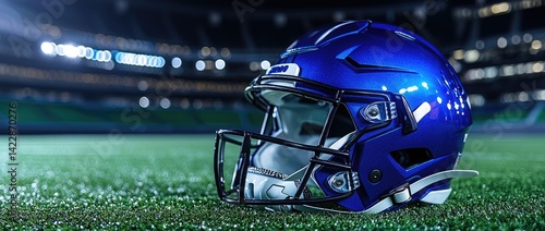 Blue football helmet on green field at night stadium.