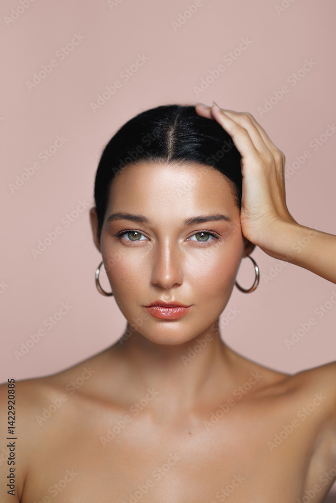 Confident young Caucasian woman with radiant, moisturized skin, wearing hoop earrings and gently holding her head. Perfect for beauty, skincare, or fashion concepts and promotions.