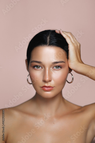 Obraz na płótnie Confident young Caucasian woman with radiant, moisturized skin, wearing hoop earrings and gently holding her head. Perfect for beauty, skincare, or fashion concepts and promotions. w salonie