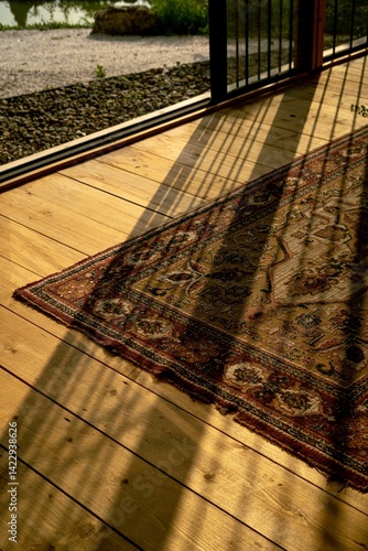 Golden light of sunset streaming through vertical bars onto a vintage Persian rug on a wooden floor