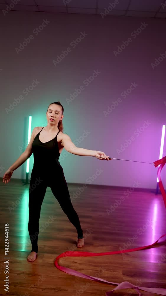 Female gymnast showcases rhythmic gymnastics routine with ribbon in vivid neon lights Female gymnast showcases rhythmic gymnastics routine with ribbon in vivid neon lights