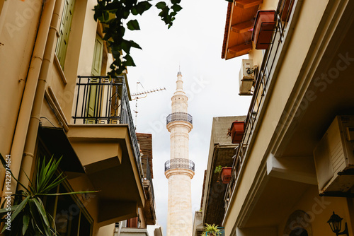 Obraz na płótnie A delightful alley bordered by historic buildings leads to an impressive minaret towering beneath a cloudy sky. Rethymno town, Crete island, Greece. w salonie