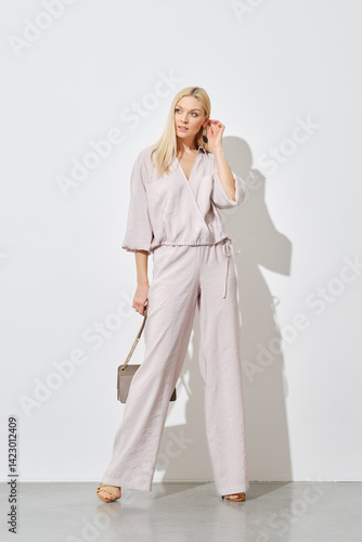 Stylish woman posing against a white wall in a wide beige blouse and trousers