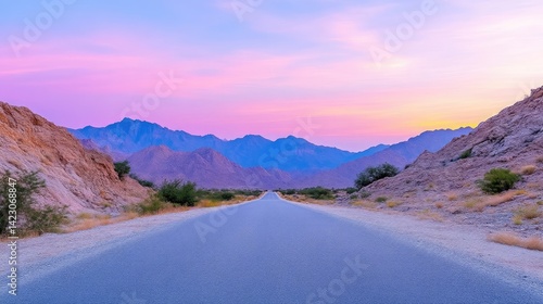 Empty road stretching into a vibrant sunset mountain vista.  Desert landscape bathed in pastel hues of pink and purple
