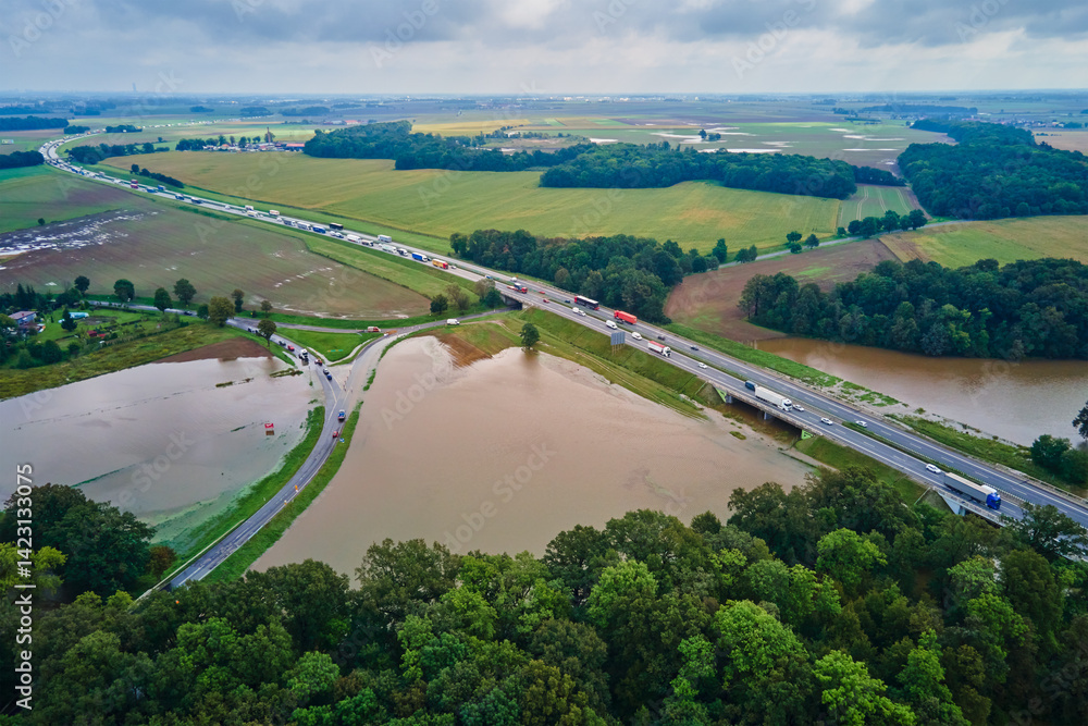 Aerial view of flooded fields and submerged rural road near busy highway. Concept of climate impact, transportation disruption and natural disaster