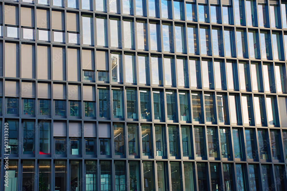 Close-up of modern office building with symmetrical glass windows and steel frames reflecting cityscape. Detail of urban architecture