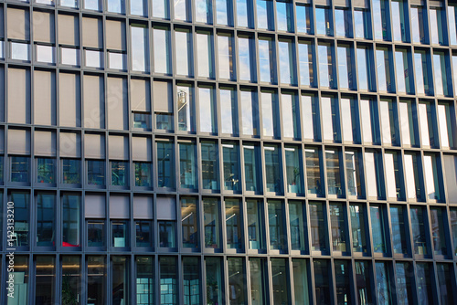 Obraz na płótnie Close-up of modern office building with symmetrical glass windows and steel frames reflecting cityscape. Detail of urban architecture w salonie