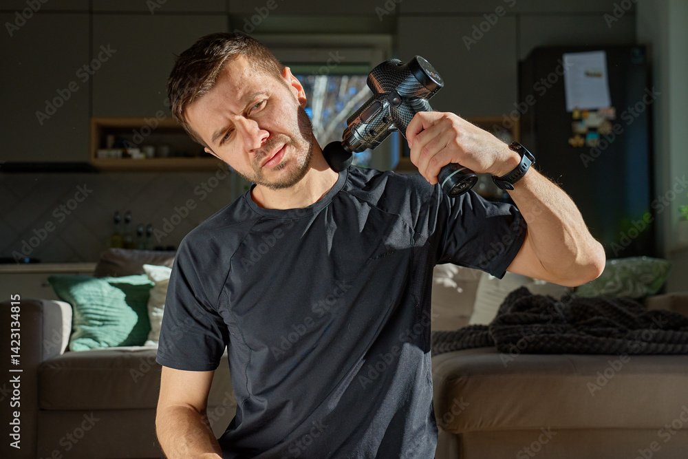 Man applies massage gun to relieve tension in neck and shoulder area. Male athlete doing self-massage therapy with percussion device for recovery after training