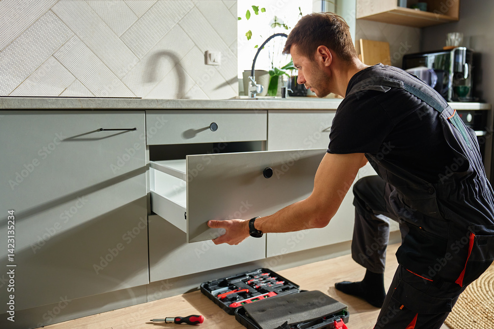 Man assembling kitchen drawer in modern cabinet using screwdriver. Handyman installing and adjusting drawer slide mechanism in contemporary kitchen. Furniture installation