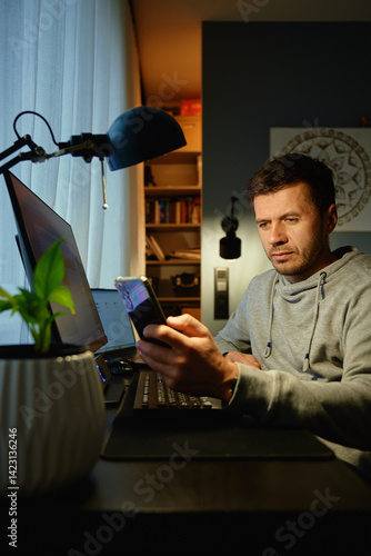 Obraz na płótnie Tired freelancer procrastinating at home office, scrolling phone instead of working. Unproductive man using smartphone at home desk. Concept of procrastination and distraction in remote work w salonie