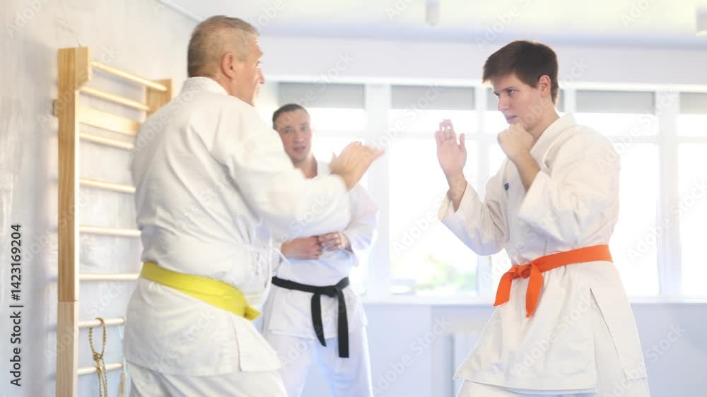 Experienced elderly karate fighter in kimono with yellow belt engaging kumite with young rival, demonstrating martial art techniques in training room Experienced elderly karate fighter in kimono with yellow belt engaging kumite with young rival, demonstrating martial art techniques in training room