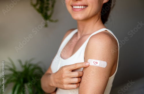 Foto Smiling woman pointing at adhesive bandage on her upper arm at vaccination site