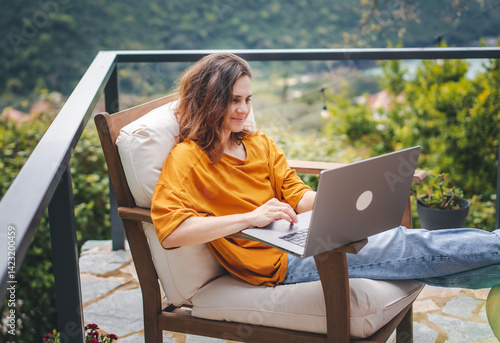 Obraz na płótnie Young woman sitting on cottage terrace using laptop in summertime, online work w salonie