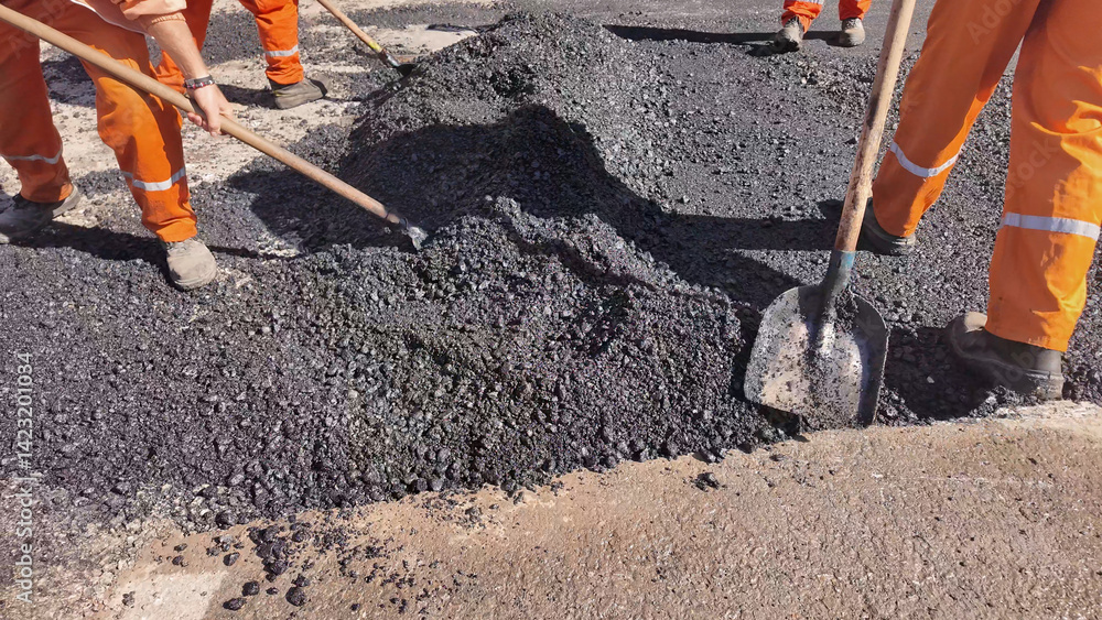 Construction workers working on a new asphalt layer on a public street.