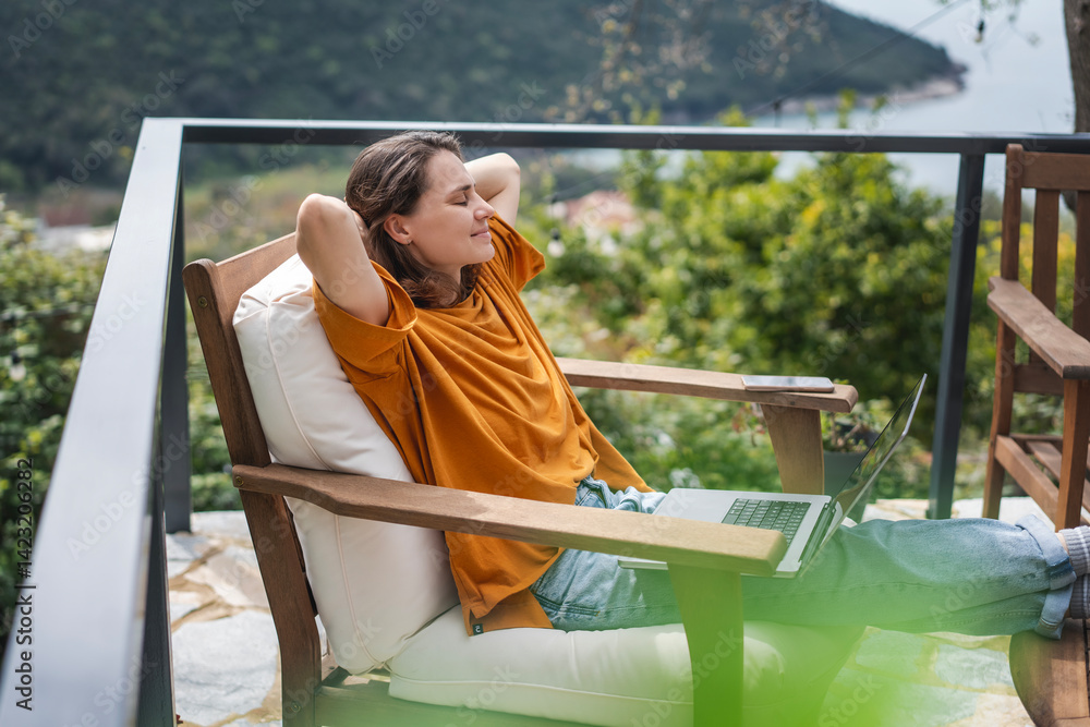 Young woman sitting on cottage terrace using laptop in summertime, online work