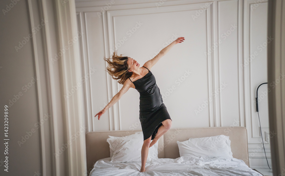 Young caucasian european happy woman in black slip dress dancing on bed, beauty fashion concept