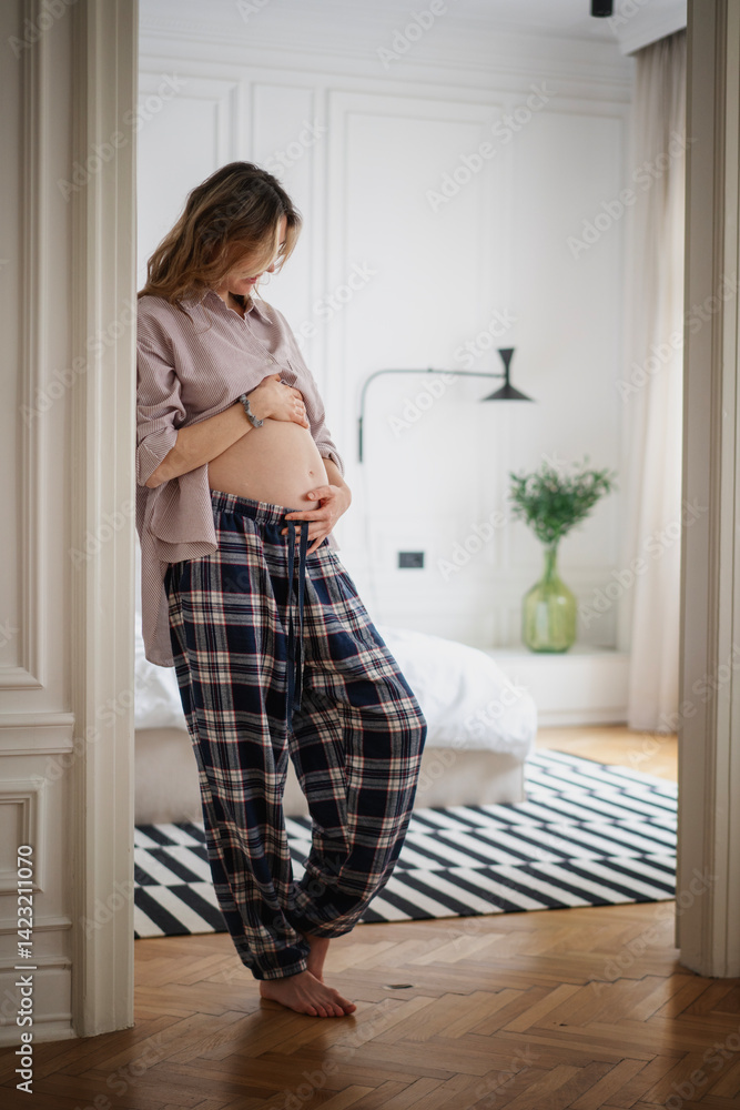 Pregnant happy woman with hands on belly stomach standing in apartment