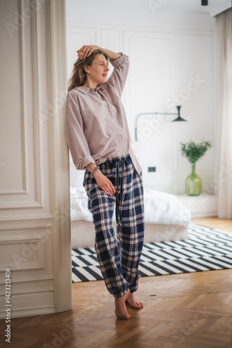 Young woman in pajamas standing at home against the background of a bedroom
