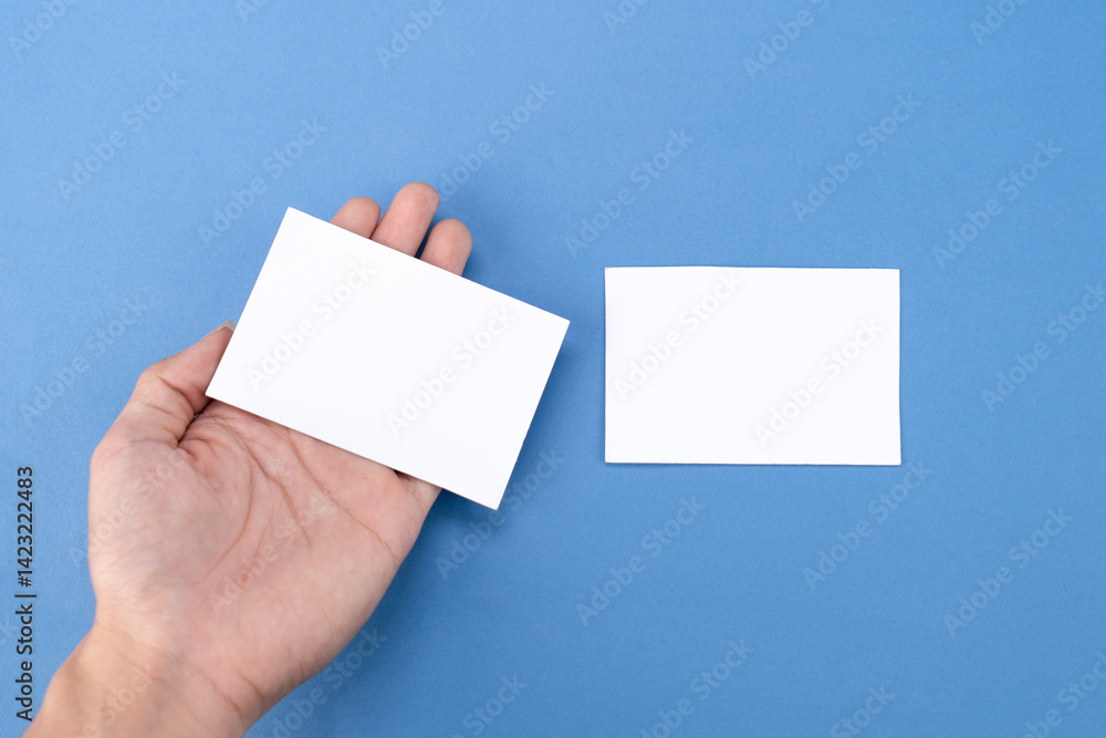 Fototapeta premium Hand holding white blank business card mockup on blue background