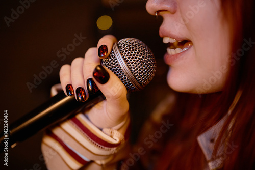 Tablou pe pânză Close up on microphone in hands of young female vocalist performing on stage