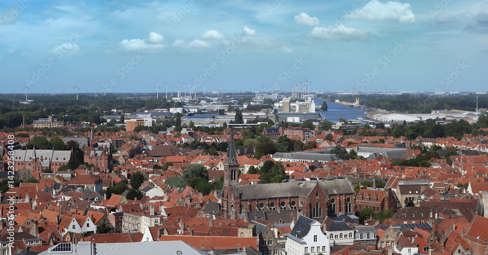 Fototapeta premium Bruges, Brugge, Belgium. Bruges cityscape with top aerial view of Bruges historical city centre with old traditional buildings red tiled roofs and dock canal with windmills on skyline horizon