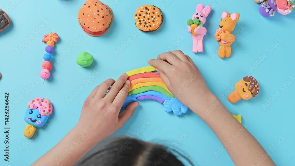 child's hands playing with colorful plasticine on blue background.