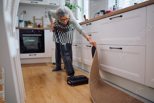 Фототапет Senior woman using vacuum cleaner in kitchen.